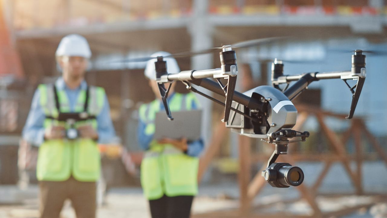 A survey drone in flight with the operator in the background
